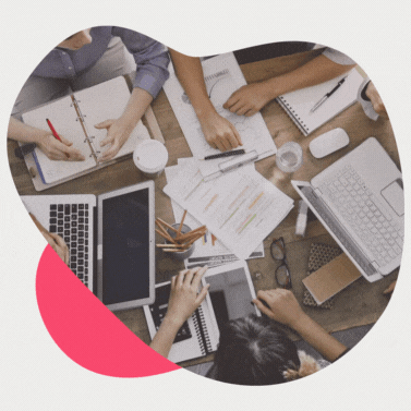 Mehrere Personen sitzen an einem Tisch mit Laptops, Papieren, Stifte und arbeiten