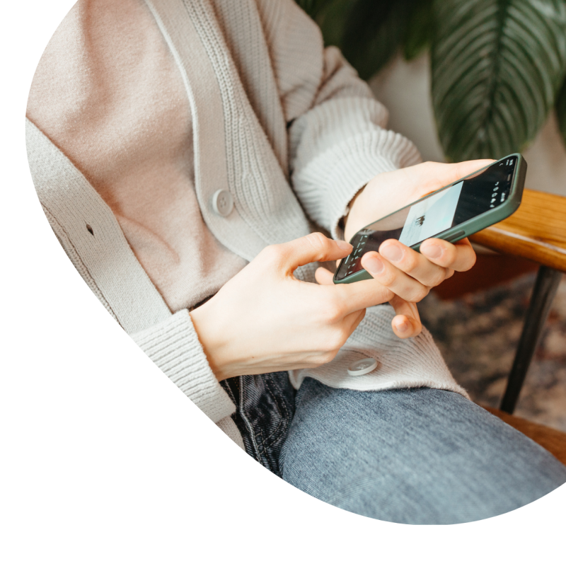 Eine Frau in Jeans und einem rosa Oberteil tippt am Handy 