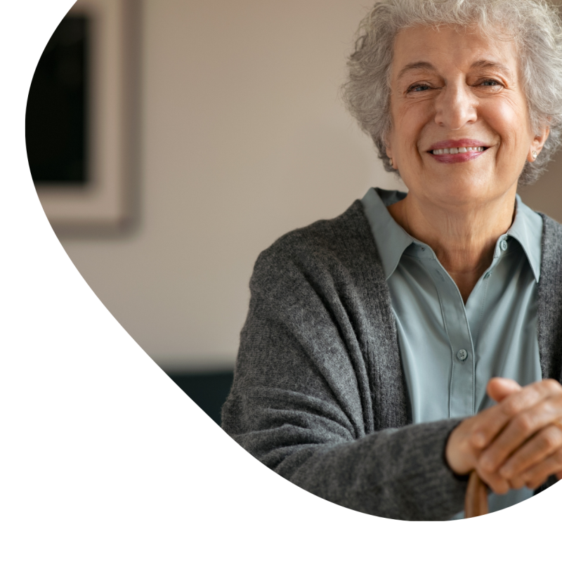 Eine Patientin in einem blauen Hemd und einer grauen Strickjacke lächelt 
