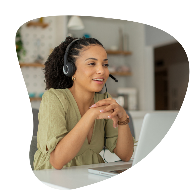 Eine Frau mit einem Headset auf dem Kopf und einem grünen Oberteil sitzt vor einem Laptop und lächelt