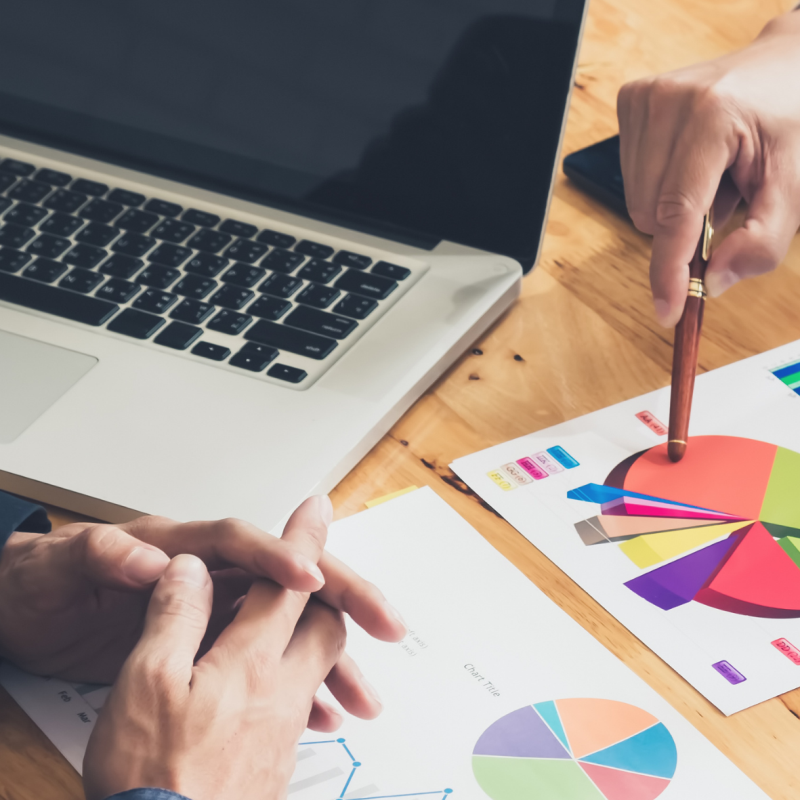 Zwei Personen sitzen an einem Tisch mit einem Laptop und Papier, dass ein Kreisdiagram abbildet